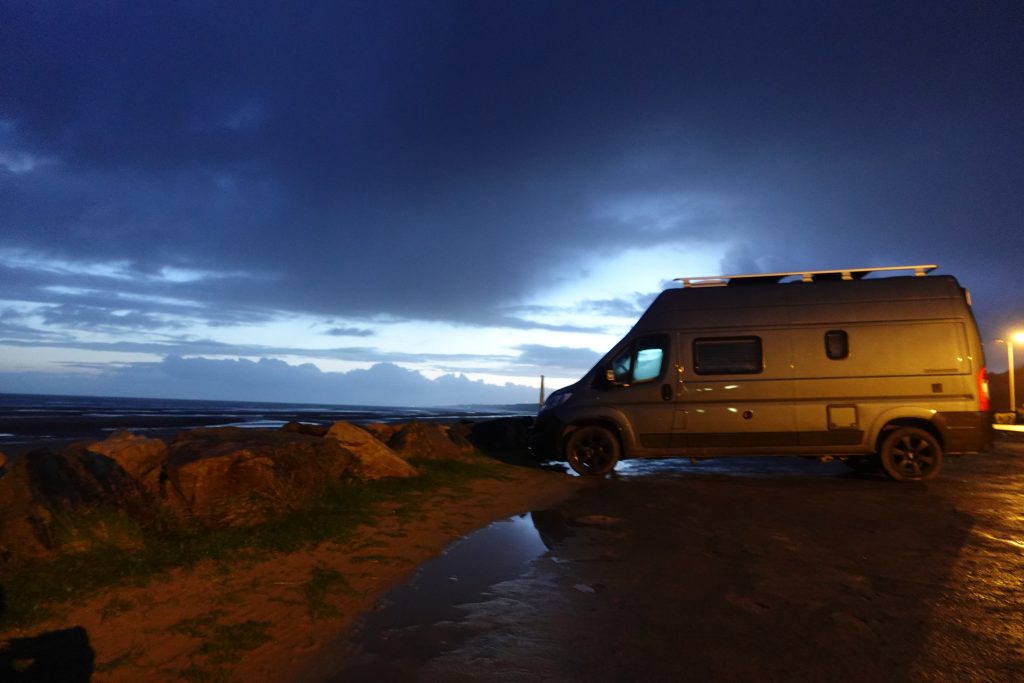 Blauer Van auf Stellplatz an Strand in Normandie