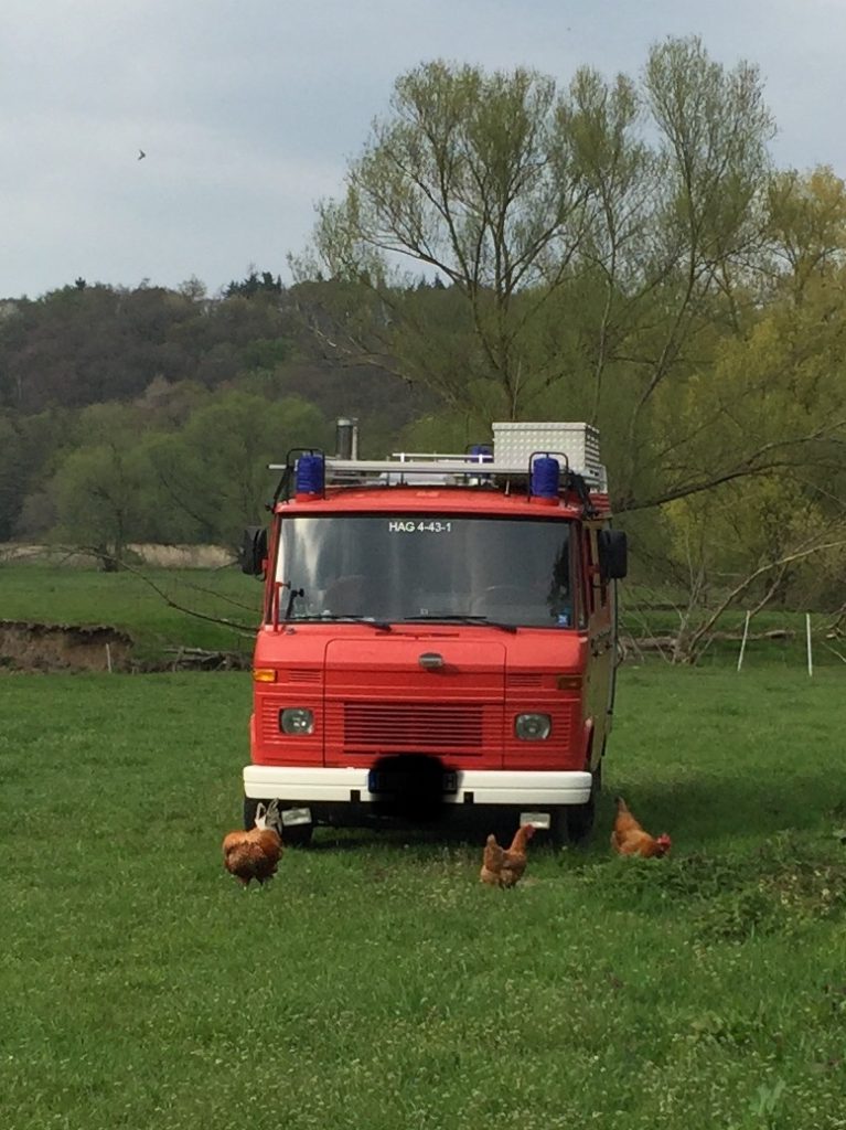 Feuerwehrwohnwagen auf einer Wiese zwischen Hühnern