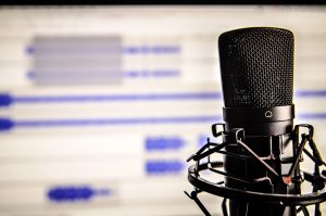 Podcast Mikofon vor einem unfokussierten Bildschirm, der Audiodateien zeigt